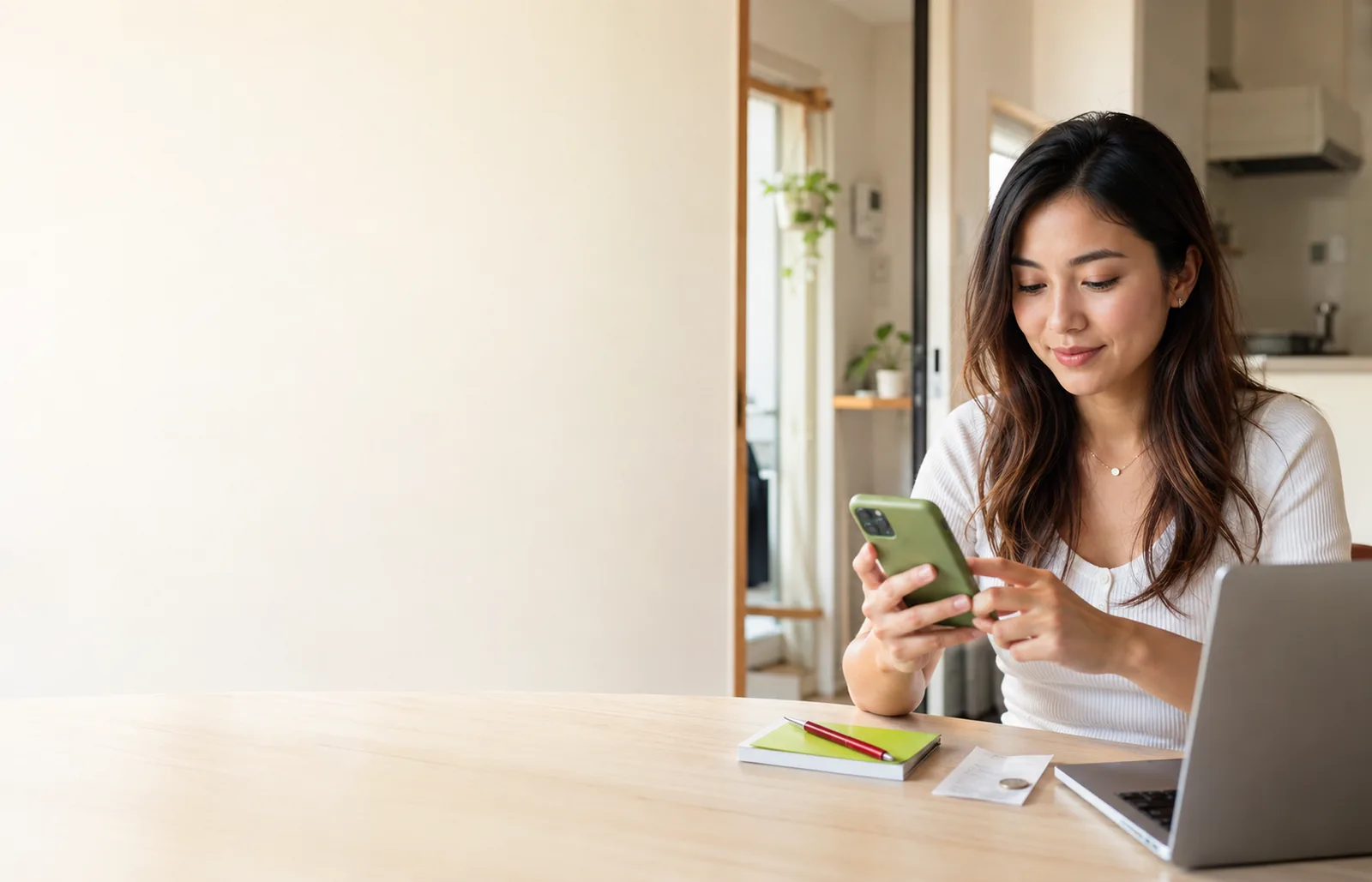 Mulher sentada à mesa usando o celular para fazer uma transferência internacional, com o notebook aberto ao lado
